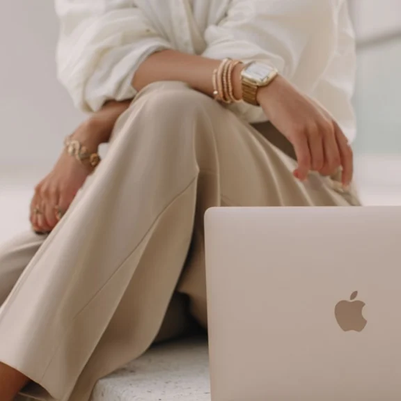 Femme élégante assise avec un MacBook représentant une formatrice esthétique indépendante