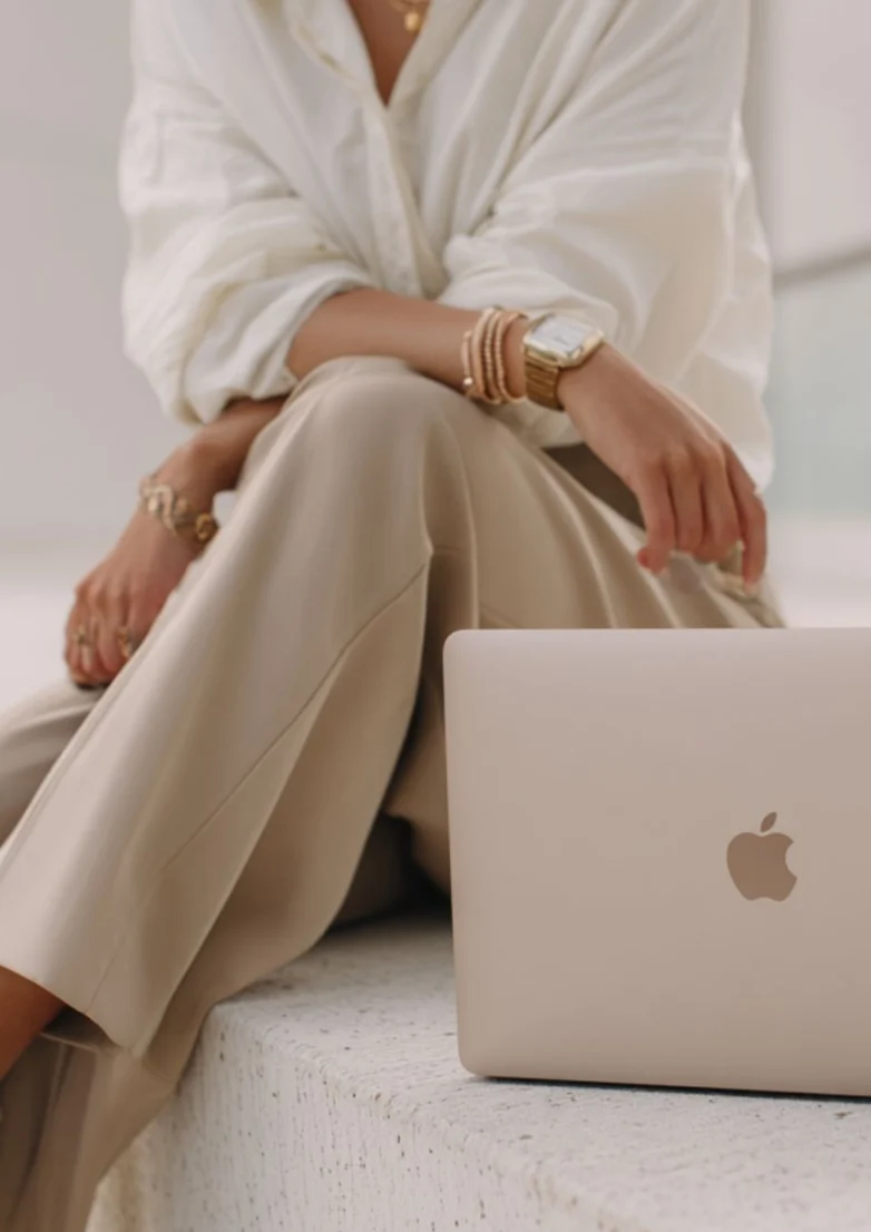 Femme élégante assise avec un MacBook représentant une formatrice esthétique indépendante